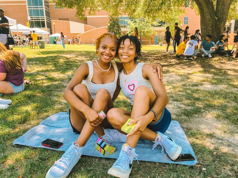 Two female students sitting on a towel playing cards outside. 